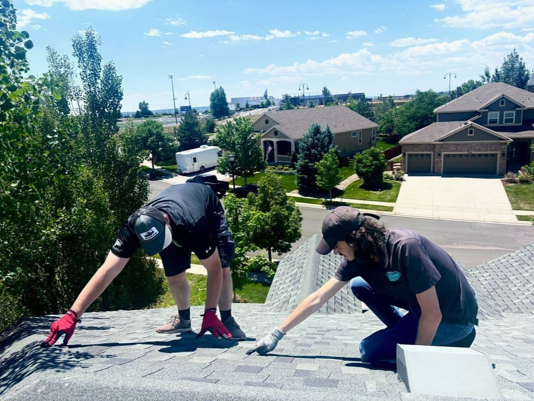 Two 1st American Roofing crew members inspecting a shingle roof in a Colorado neighborhood